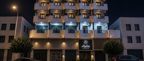 A multi-story hotel with balconies, a sign reading 'Ayliz City Hotel,' and two cars parked in front.