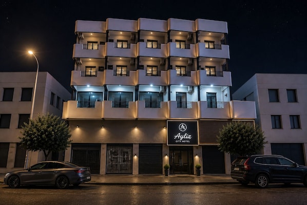 A multi-story hotel with balconies, a sign reading 'Ayliz City Hotel,' and two cars parked in front. - Ayliz City Otel (Manavgat)