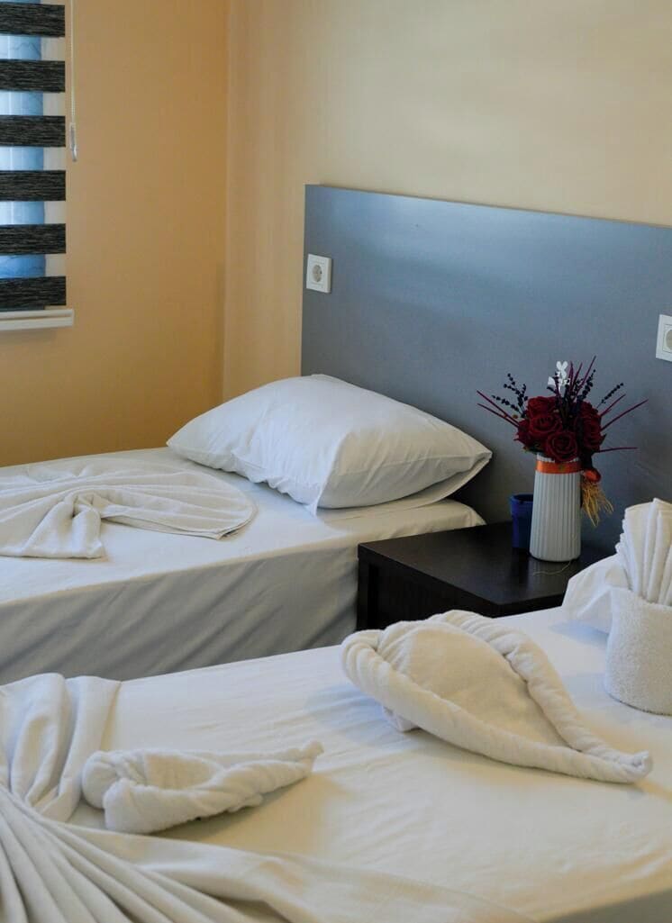Habitación de hotel con dos camas, una mesita de noche, un florero y una ventana con persianas.