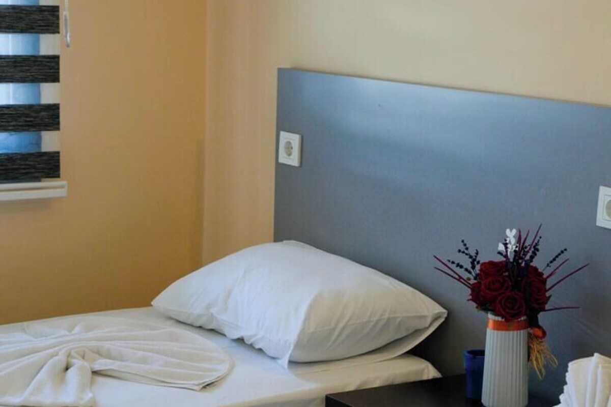 A hotel room with two beds, a nightstand, a vase with flowers, and a window with blinds.