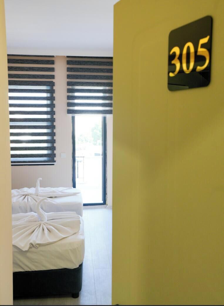 Habitación de hotel con cama, ventana con persianas y un cartel en la pared con el número 305.