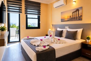 A hotel room with a bed, a view of the city, a painting of ancient columns, and a balcony with a plant. - Ayliz City Otel (Manavgat)