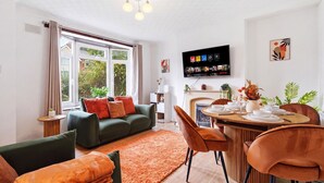 A modern living room with a green sofa, orange cushions, a dining table set for four, and a TV mounted on the wall. - Crew Comfort Walsall | Sleeps 6 | Fast Wi-Fi (Walsall)
