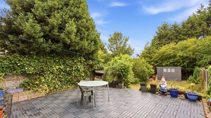 A patio with a table and chairs, surrounded by dense greenery and a small shed. - Crew Comfort Walsall | Sleeps 6 | Fast Wi-Fi (Walsall)