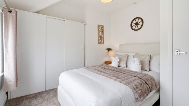 A bedroom with a large bed, a wardrobe, a nightstand with a lamp, and a decorative wall piece. - Crew Comfort Walsall | Sleeps 6 | Fast Wi-Fi (Walsall)