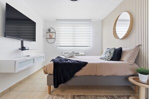 A modern bedroom with a bed, a TV, a window with blinds, a bedside table, and a mirror. - AQUATIKA!!!5 Pools, Hot Tubs, Lazy River, Beach, Tennis, Mini golf, pickleball (Mediania Alta)