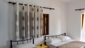 A bedroom with two beds, a nightstand, and a window with curtains.