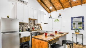 A kitchen with white cabinets, a wooden ceiling, and a small island with stools. - Cute Farm 1 Cozy 2-bedroom cottage in lovely St. Cloud with AC (St. Cloud)