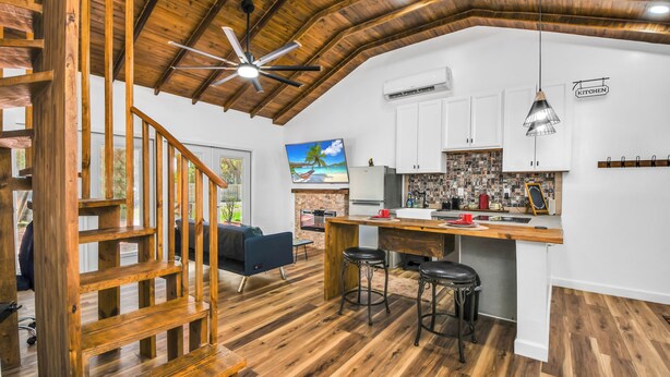 A spacious kitchen with a wooden ceiling, white cabinets, and a bar area with stools. - Cute Farm 1 Cozy 2-bedroom cottage in lovely St. Cloud with AC (St. Cloud)