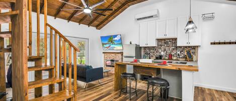 A spacious kitchen with a wooden ceiling, white cabinets, and a bar area with stools.