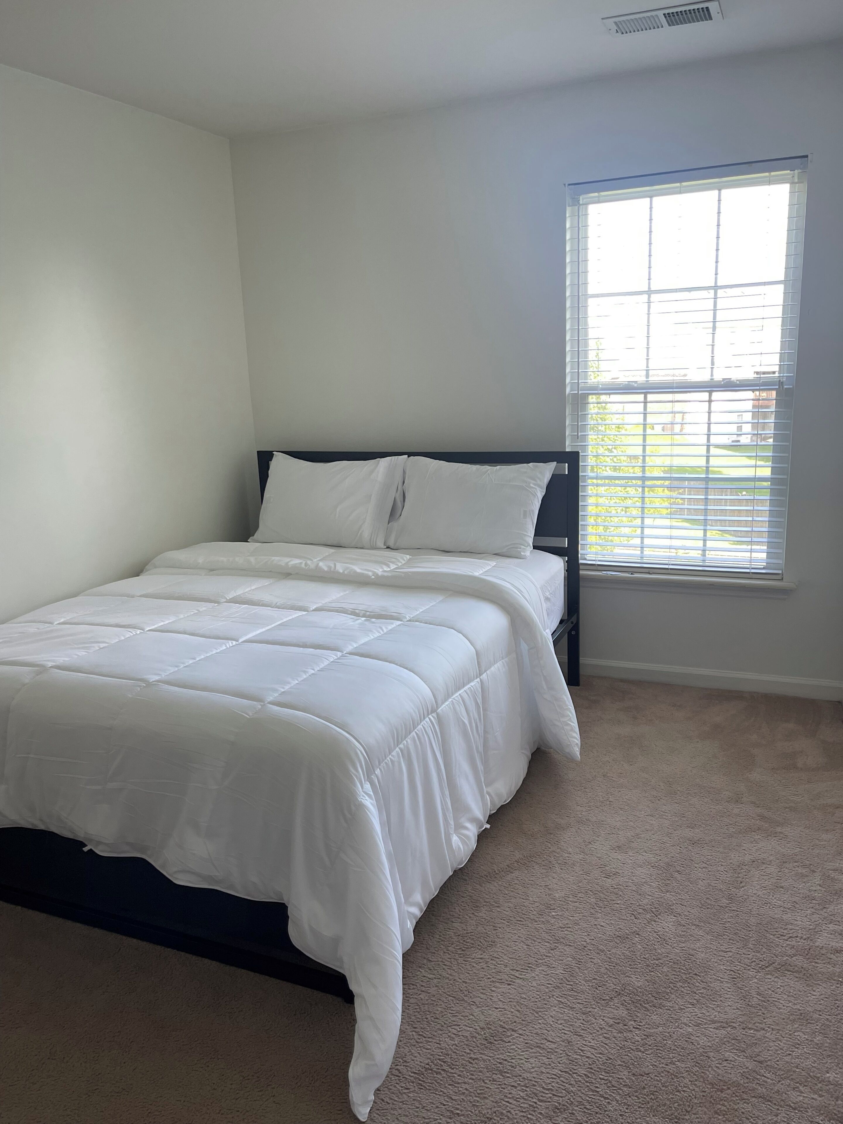 Un dormitorio con cama, ventana y piso alfombrado.