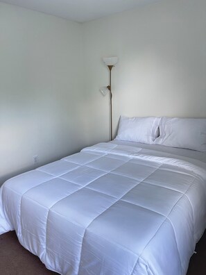 A bedroom with a bed, white bedding, a floor lamp, and a plain wall. - Peaceful 4-bedroom house with AC in charming Lexington (Lexington)