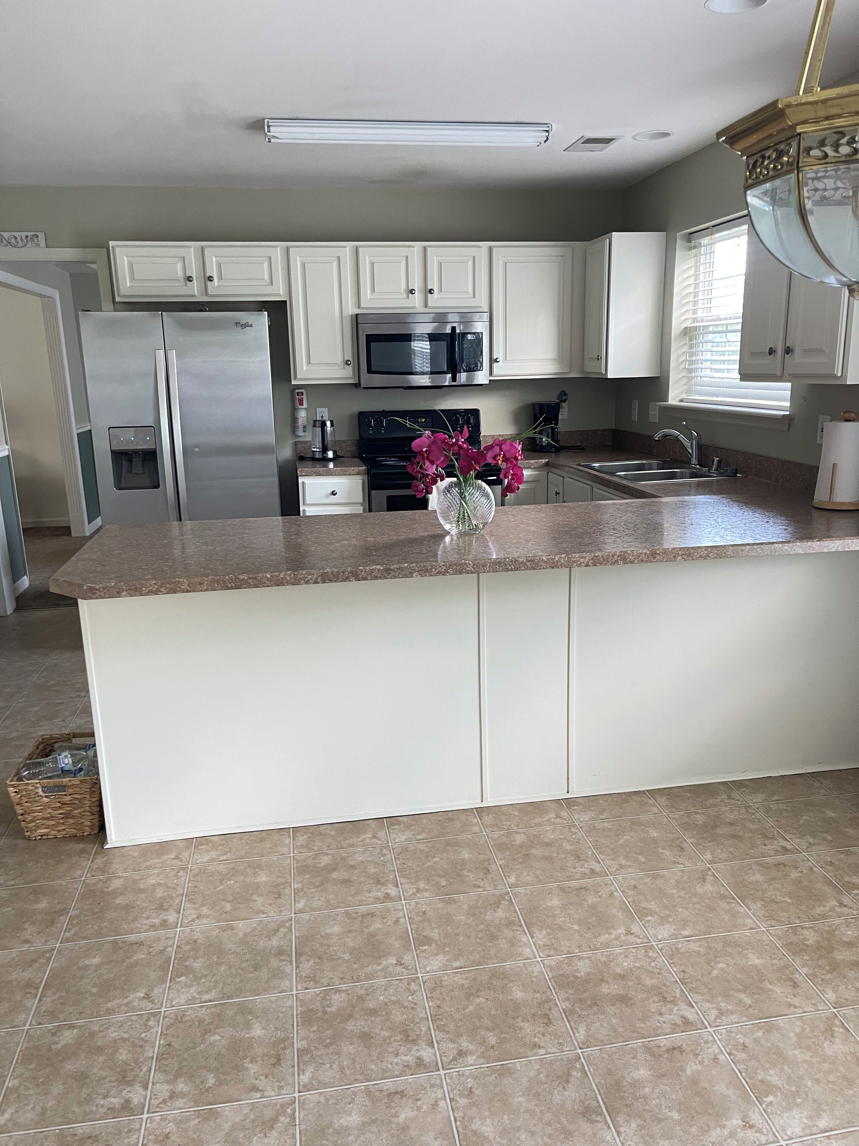 A kitchen with white cabinets, stainless steel appliances, a granite countertop, and a vase with flowers.