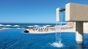 Une piscine à débordement offrant une vue sur l’océan, des chaises longues et des parasols.