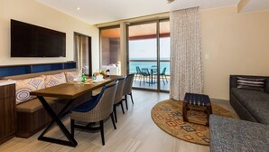 Une chambre d’hôtel moderne dotée d’un coin repas, d’un canapé, d’une télévision et d’un balcon offrant une vue sur la mer.