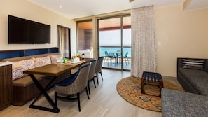 Ein modernes Hotelzimmer mit Essbereich, einer Couch, einem Fernseher und einem Balkon mit Meerblick.
