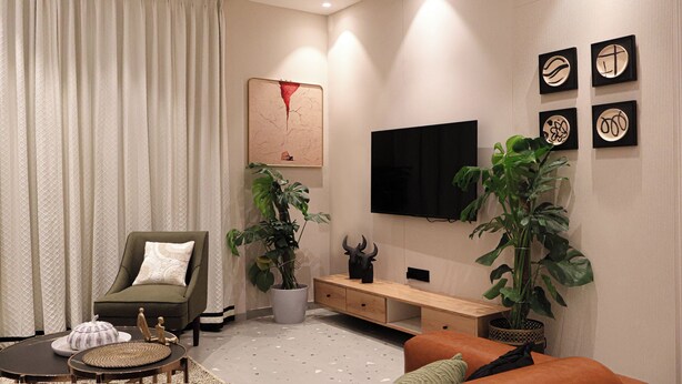 Ein modernes Wohnzimmer mit Sofa, Couchtisch, Wandfernseher und Zierpflanzen.