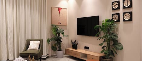 A modern living room with a sofa, a coffee table, a TV mounted on the wall, and decorative plants.