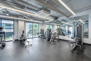 Un gimnasio moderno con diverso equipo de ejercicio, amplias ventanas y un diseño industrial limpio.