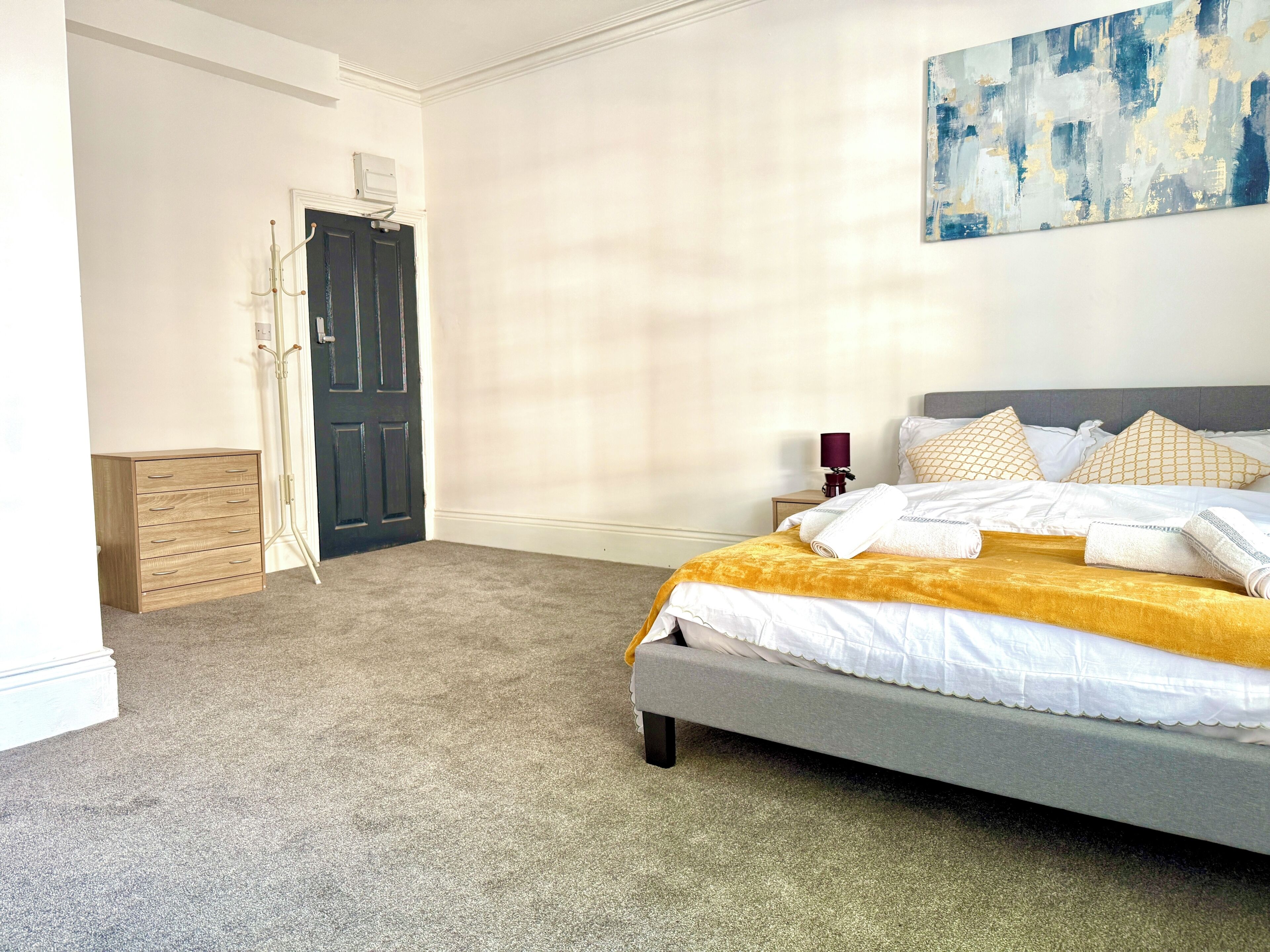 A bedroom with a bed, a nightstand, a lamp, a door, and a coat rack.
