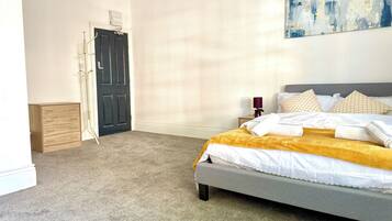 A bedroom with a bed, a nightstand, a lamp, a door, and a coat rack.