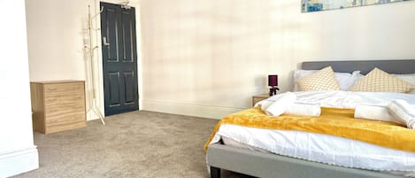 A bedroom with a bed, a nightstand, a lamp, a door, and a coat rack.