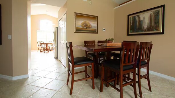 A dining area with a wooden table and chairs, a painting on the wall, and a view into another room. - 3Bed/2Bath Lakeside Tranquility (Kissimmee)