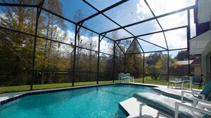 A swimming pool with a glass enclosure, surrounded by lounge chairs and a grassy area. - 3Bed/2Bath Lakeside Tranquility (Kissimmee)