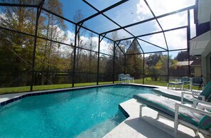 Ein Schwimmbecken mit Glasveranda, umgeben von Liegestühlen und einer Rasenfläche.