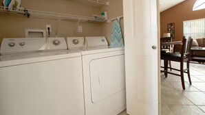 A laundry area with a washing machine, dryer, and shelves with laundry items. - 3Bed/2Bath Lakeside Tranquility (Kissimmee)
