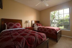 Ein Schlafzimmer mit zwei Betten, einem Deckenventilator, einem Fenster mit Jalousien und einem Nachttisch mit Lampe.