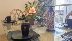 Ein Essbereich mit einem Glastisch, schwarzen Tassen auf Untersetzern und einer dekorativen Vase mit Blumen.