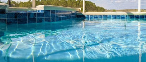 Une piscine intérieure à eau claire, avec des murs carrelés et une vue sur les arbres en arrière-plan.