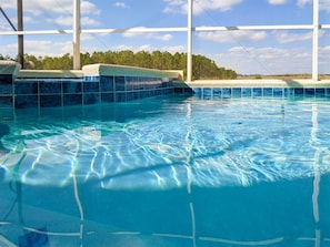 A clear indoor swimming pool with tiled walls and a view of trees in the background. - Newly Remodeled Home with a Private Pool and Hot Tub, Right Next to Disney! (Davenport)