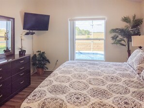 A bedroom with a large bed, a TV mounted on the wall, a window with a view of a swimming pool, and a potted plant. - Newly Remodeled Home with a Private Pool and Hot Tub, Right Next to Disney! (Davenport)
