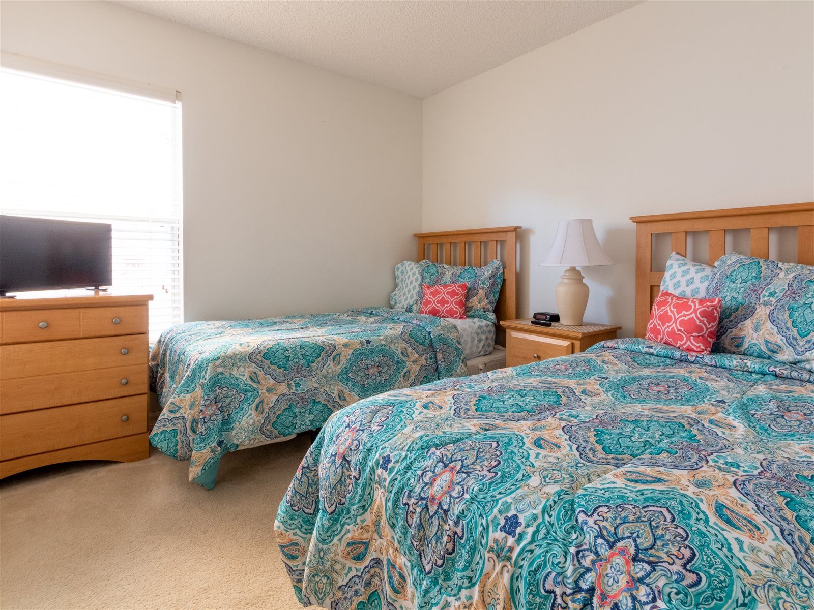 A bedroom with two beds, a dresser, a lamp, and a television.