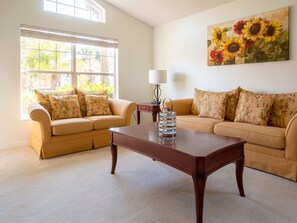 A living room with two beige sofas, a wooden coffee table, and a painting of sunflowers on the wall. - Resort Community, Private Pool and Hot Tub, Right Next to Disney! (Kissimmee)