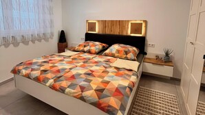 Een slaapkamer met een bed, nachtkastjes, een wandplank en een raam met gordijnen.
