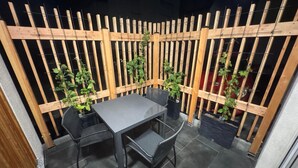 Een klein terras buiten met een tafel en stoelen, omgeven door een houten omheining en plantenpotten.