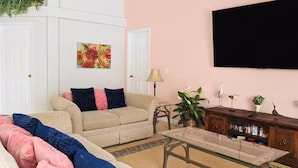 A living room with a beige sofa, a glass coffee table, and a television on the wall. - 4Bed/3Bath Sunny Lakeview Escape (Davenport)