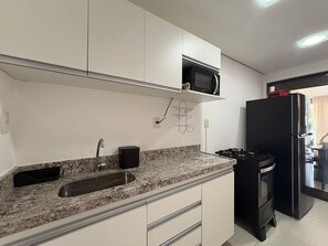 Een keuken met een granieten aanrecht, een roestvrijstalen spoelbak, een zwarte koelkast en een magnetron boven het fornuis.