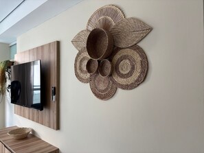 Ein an der Wand befestigter Fernseher und ein dekoratives Wandbild mit Gewebestruktur.