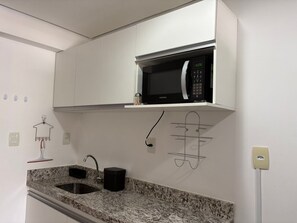 A kitchen with white cabinets, a granite countertop, a black microwave, and a sink. - Flamboyant Bessa Flat  (João Pessoa)