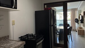 A compact kitchen with a gas stove, a black refrigerator, and a microwave. - Flamboyant Bessa Flat  (João Pessoa)