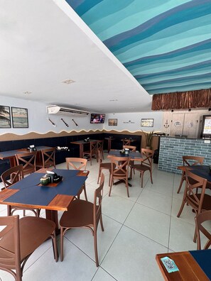 Ein Restaurant mit Sitzecken und Tischen, einem Fernsehbildschirm und einem Wandgemälde an der Decke.