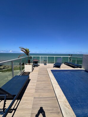 Ein Poolbereich mit Liegestühlen und Blick auf das Meer.