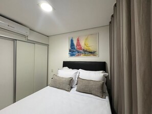 Ein Hotelzimmer mit einem Bett, einem Segelbootgemälde, einem Fenster mit Vorhängen und einer Klimaanlage.