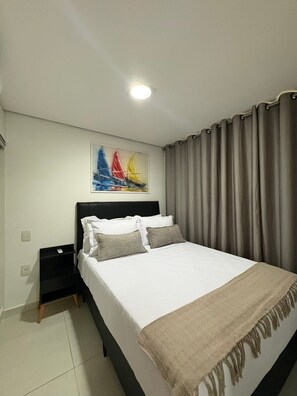 Een slaapkamer met een bed, nachtkastje, wanddecoratie en een raam met gordijnen.