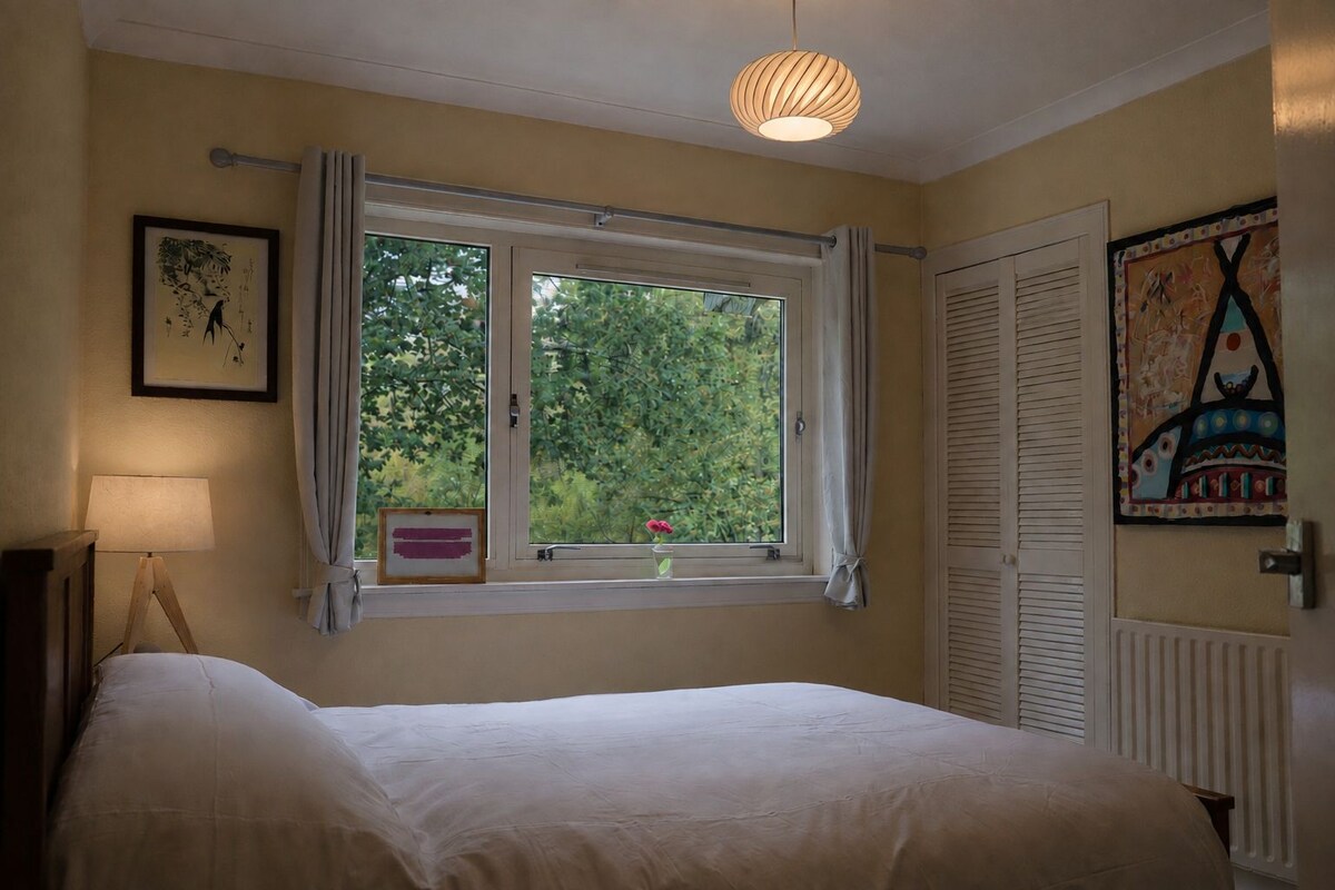 Quarto com cama, janela com cortinas, luminária de cabeceira e quadro na parede.