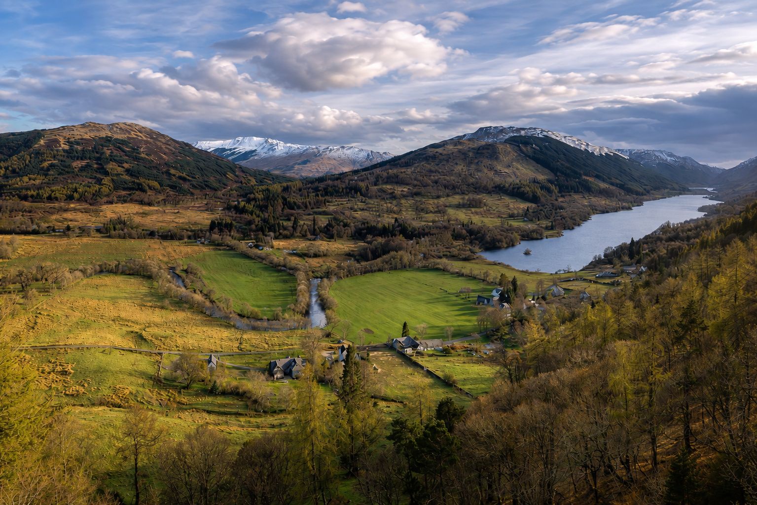 A mountainous landscape with a river, fields, and a lake.